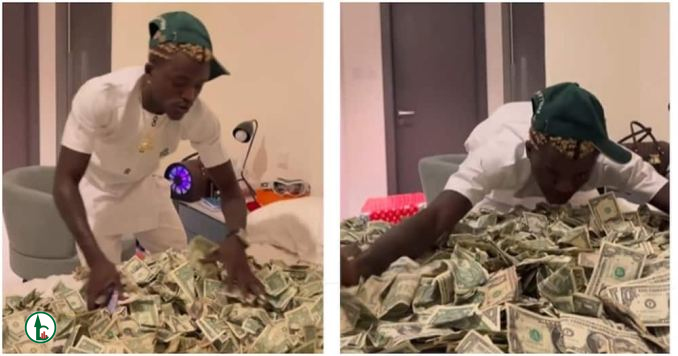 Portable prays for fans as he shows off foreign money he received on a bed Nigeria